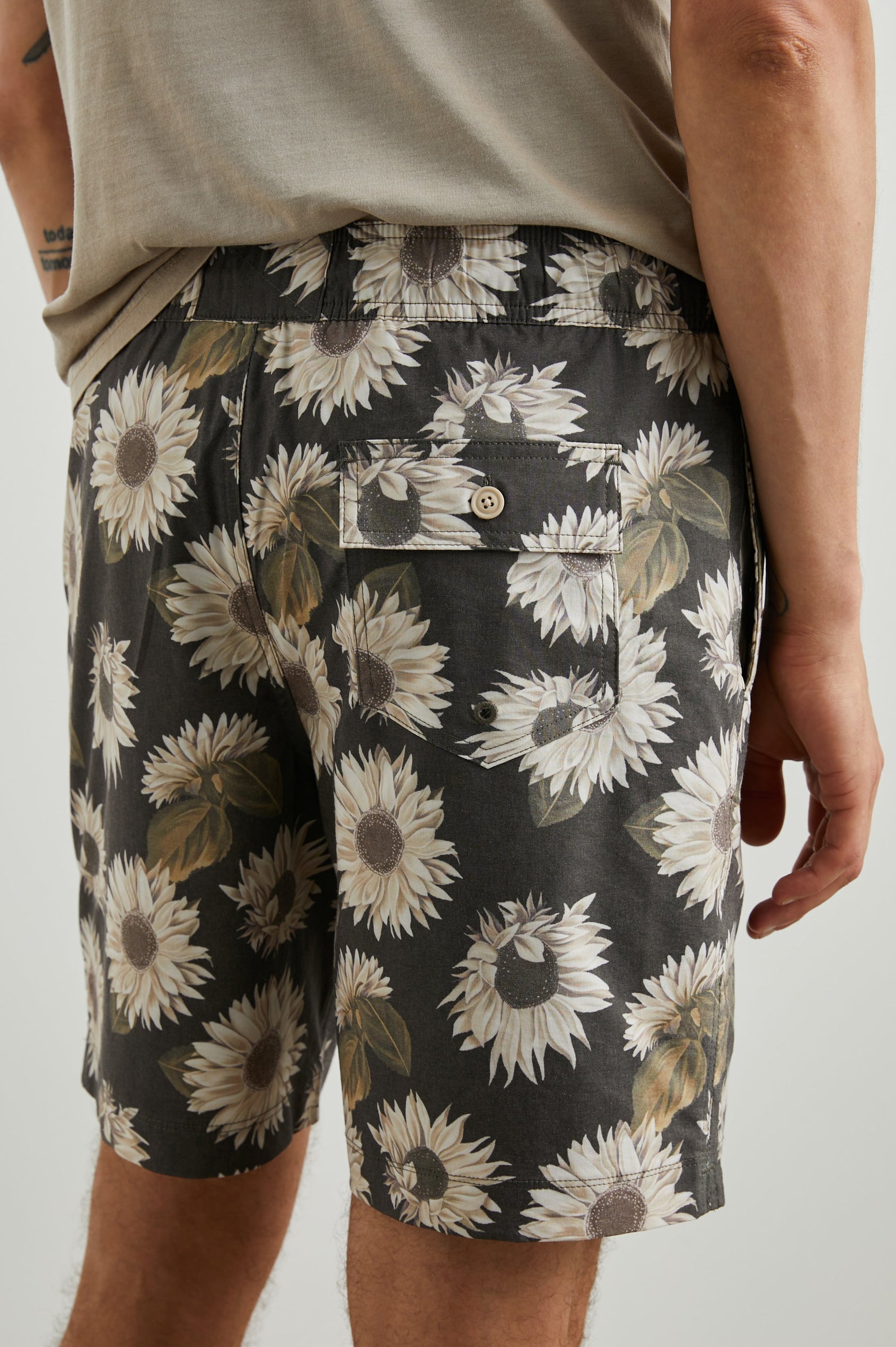 Kian Swim Shorts with an Elastic Drawstring Waistband, Two Front Pockets and a Back Button Flap Pocket in Sunflower Twirl Black Colorway, Sunflowers on Black - Back View Featured on Model