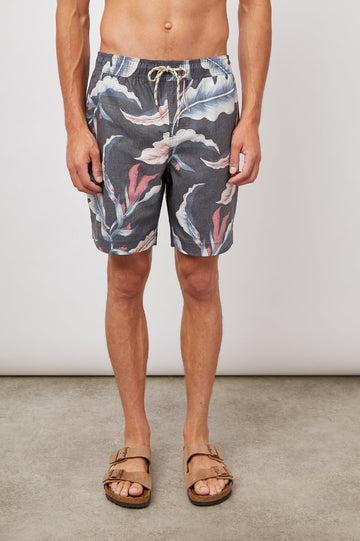 Kian Swim Shorts with an Elastic Drawstring Waistband, Two Front Pockets and a Back Button Flap Pocket in Paradise Nights Colorway, a Floral Print in Pinks, Blues and White on Black - Front View Featured on Model