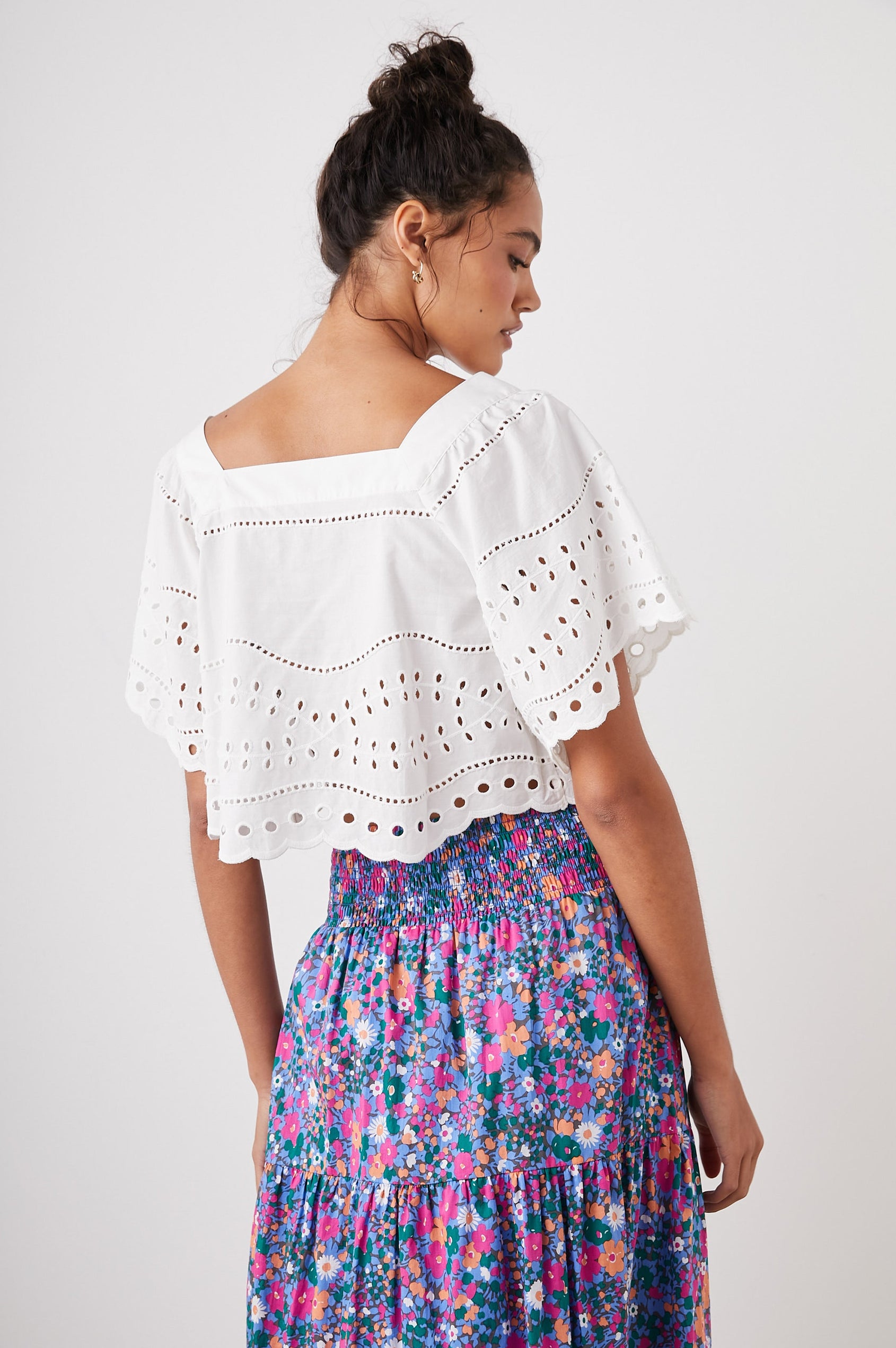 Kit Short Sleeve Crop Top with a Square Neckline, Front Button Closure, and an Eyelet Design in White Eyelet Embroidery Colorway - Back View Featured on Model 