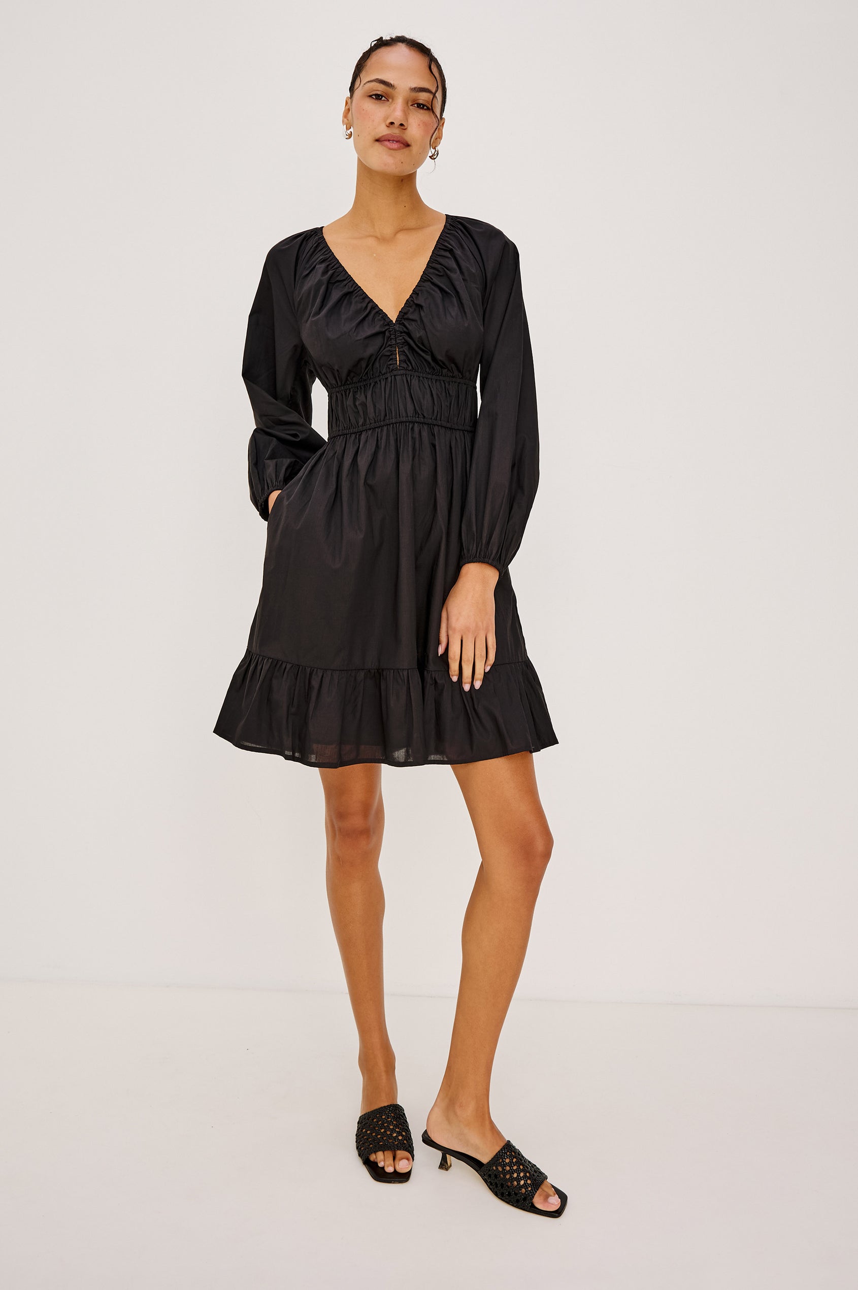 Krina Mini Dress in Cotton Poplin With Deep V-Neckline, Center Front Ties, Long Billowing Sleeves, and Tiered Hem in Black Colorway - Full Body Front View Featured on Model