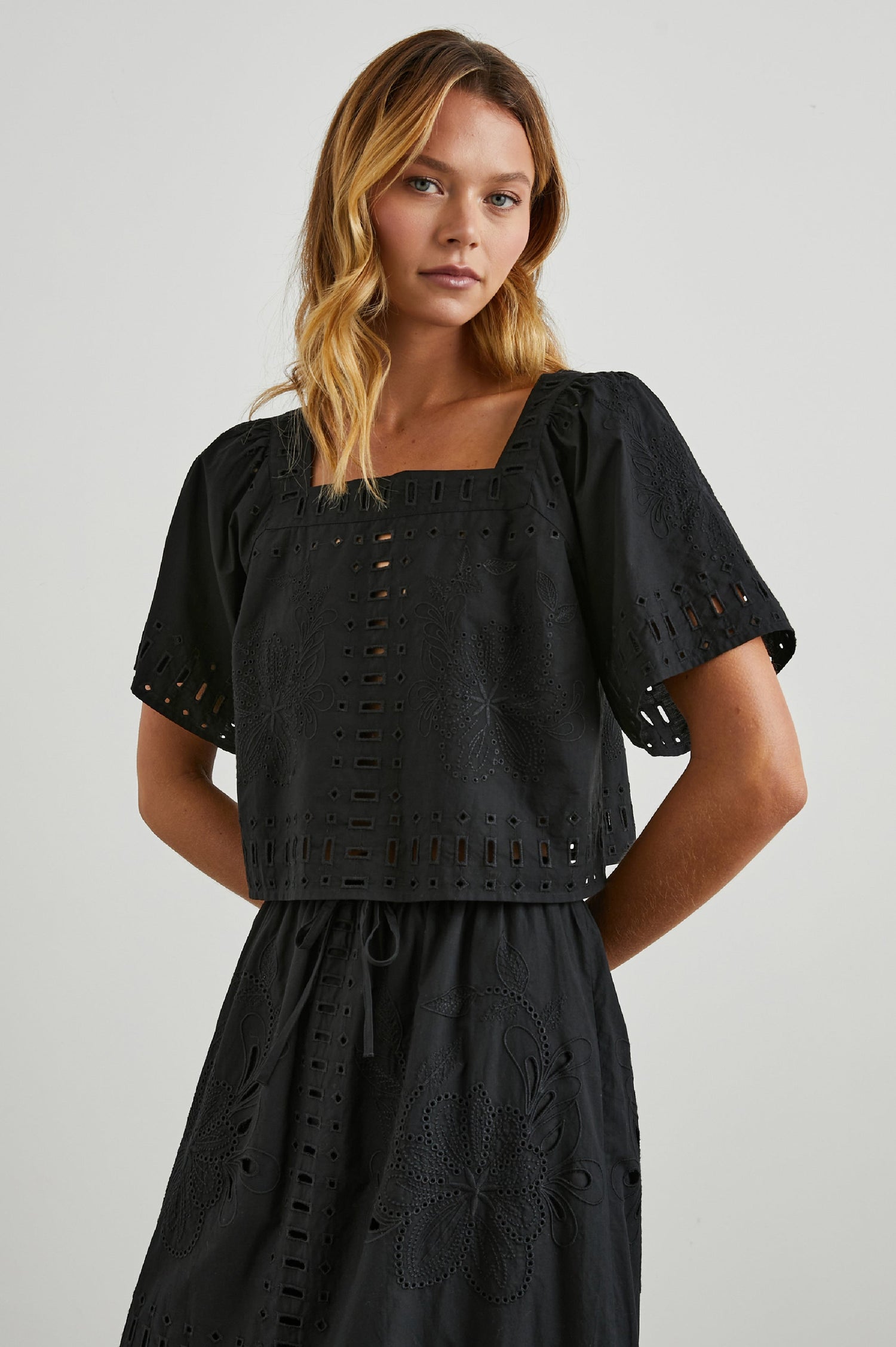 Laine Short Sleeve Crop Top with Square Neckline, and a Floral and Geometric Eyelet Design in Black Colorway - Front View Featured on Model