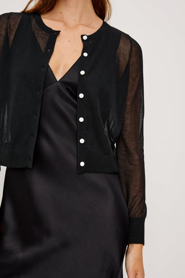 Lakelyn is a sheer button front cardigan with ribbed trim in black colorway. Front detail view featured on model.