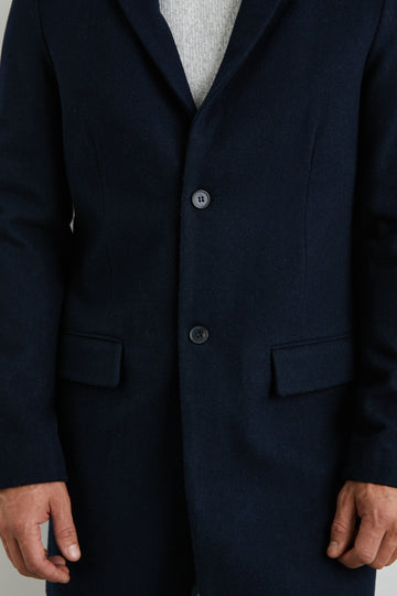 Lark Thigh-Length Coat with Two Button Closure, Notched Lapels, and Two Front Flap Pockets in Navy Colorway - Front View Featured on Model