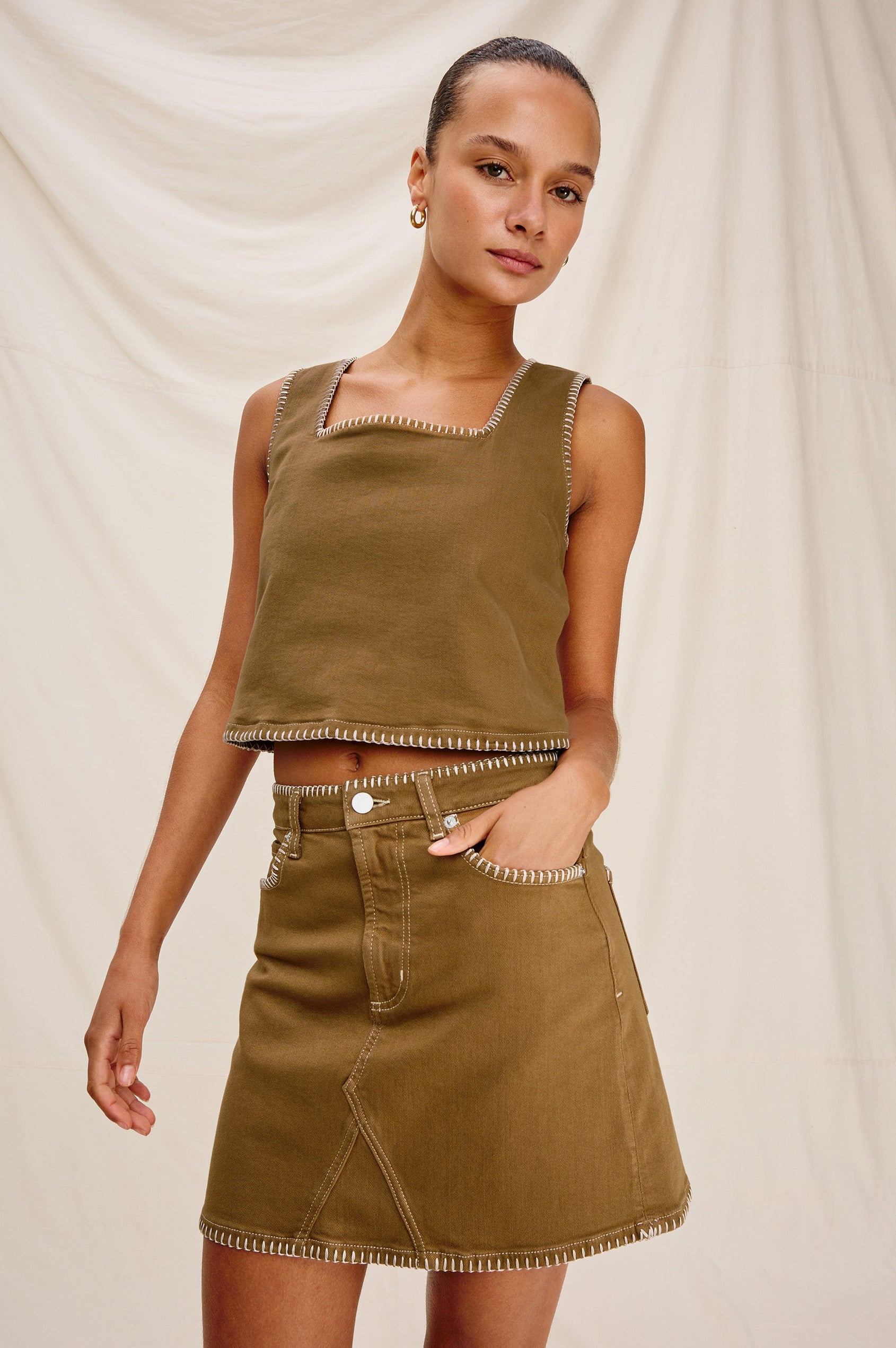 Laurel 5-Pocket Colored Denim Mini Skirt With Blanket Stitch Along All Edges in Safari Embroidered. Front View Shown on Model.