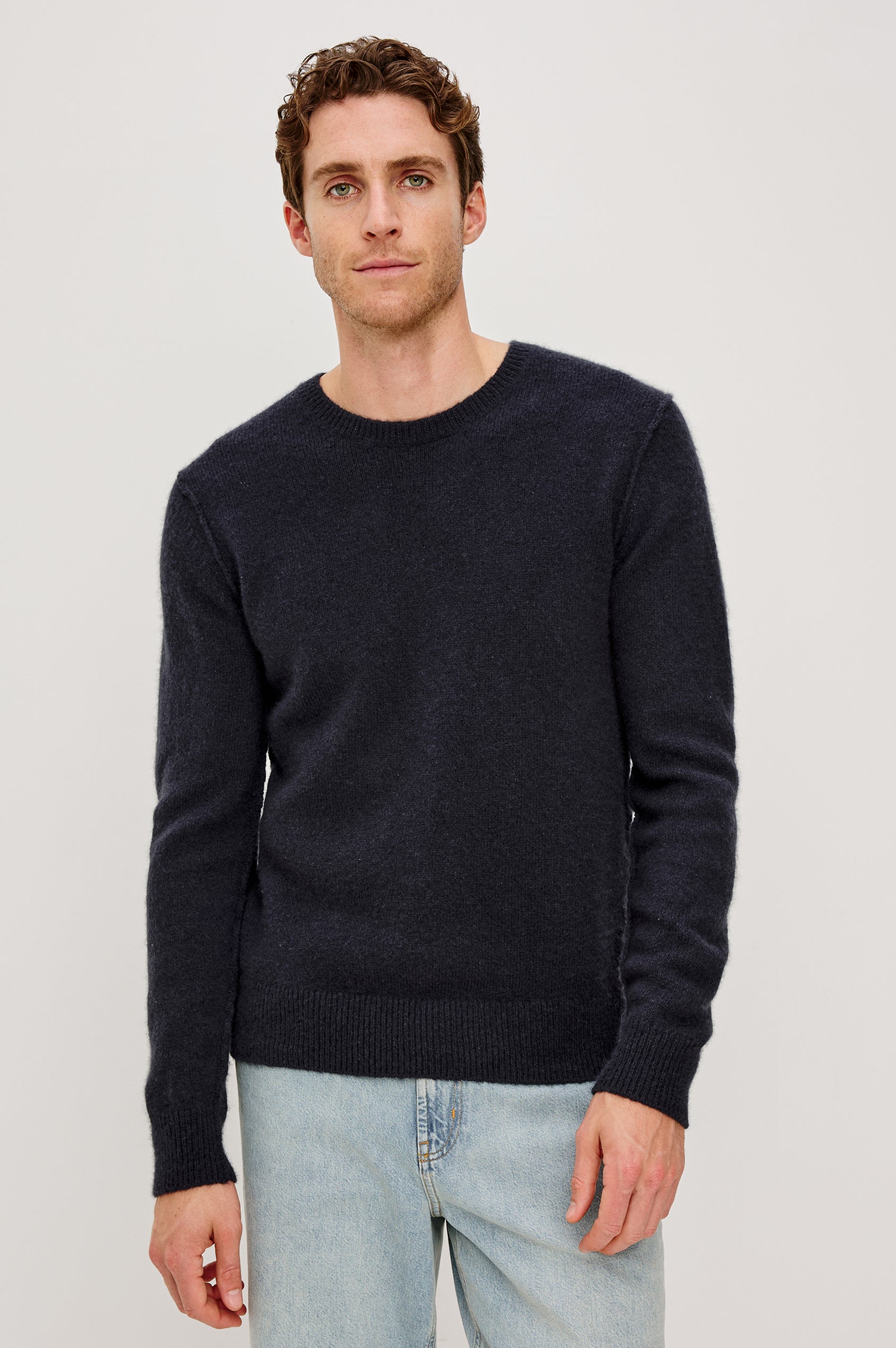 The Laurent is a relaxed-fit sweater with dropped shoulders, long sleeves, and linking-stitch detailing at the shoulders in Midnight colorway. Front view featured on model.