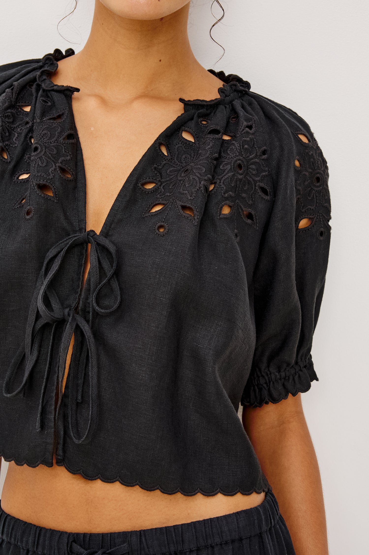Lizbeth Milkmaid Top in Linen With Floral Eyelet Cutwork Plunging Tie-Front V-Neckline Front Ties Relaxed FIt Short Puff Sleeves in Black Ctolorway - Upper Body Front View Featured on Model