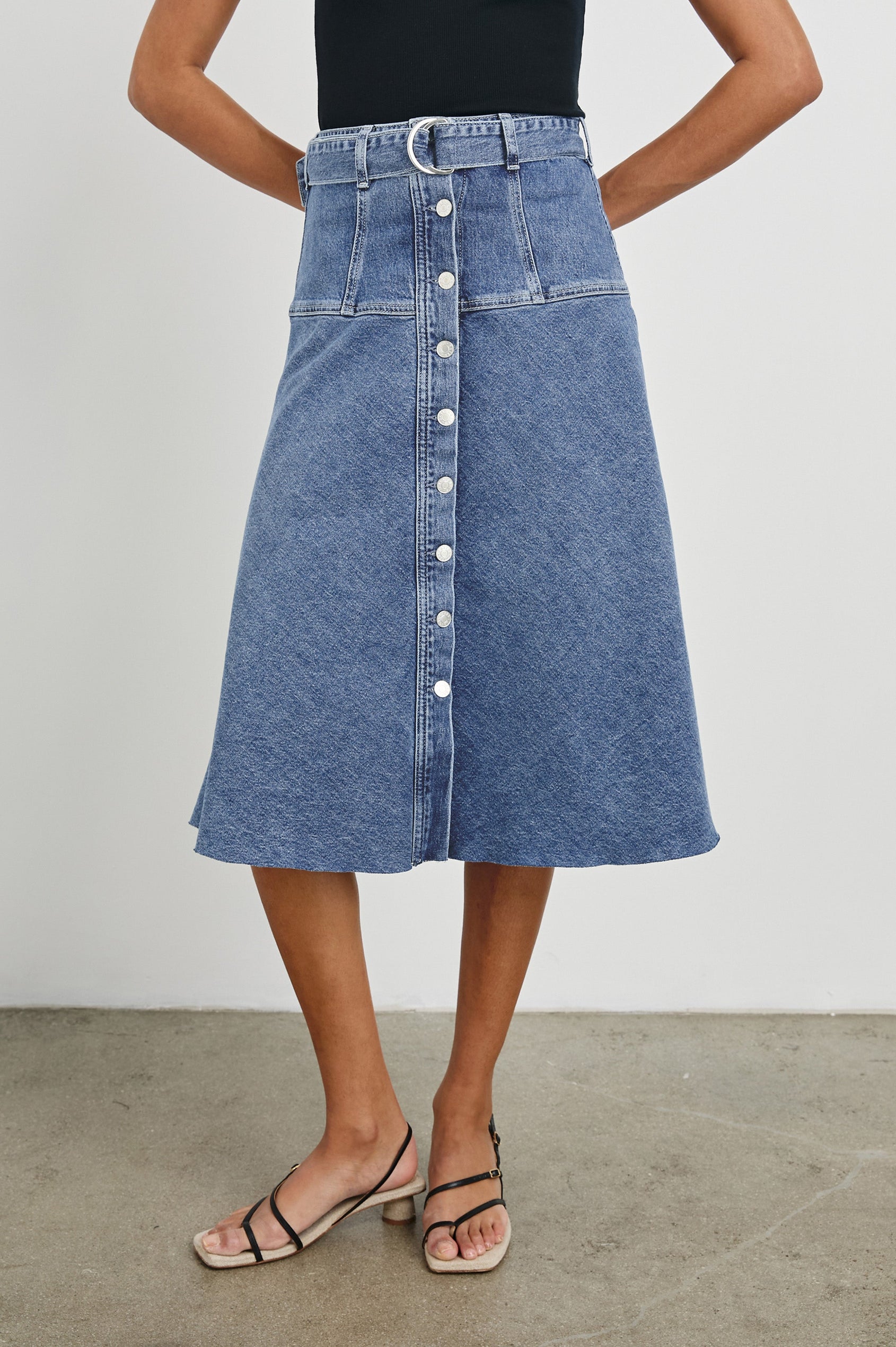 Loma Below-Knee A-Line Denim Skirt with an Exposed Button Front Opening, Adjustable Self Belt with D-Ring Closure and a Raw Hem in Pacific Coast Colorway. Front View Shown on Model.