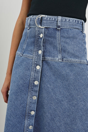 Loma Below-Knee A-Line Denim Skirt with an Exposed Button Front Opening, Adjustable Self Belt with D-Ring Closure and Stitching Details on Waist/Hip in Pacific Coast Colorway. Front Detailed View Shown on Model.