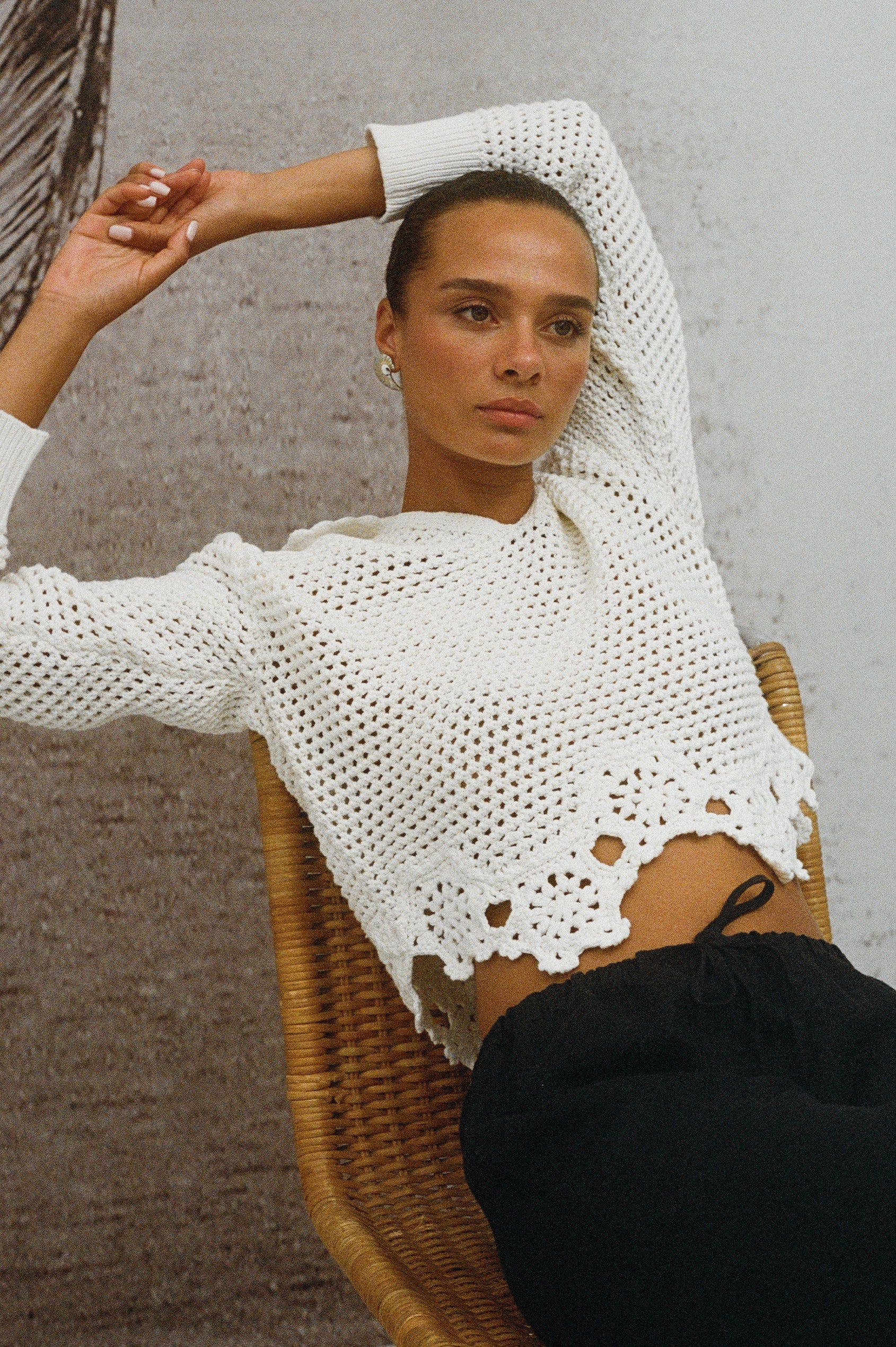 Louise open knit crochet sweater in Ivory with solid knit collar and floral scalloped hem - on model sitting on chair, arms up
