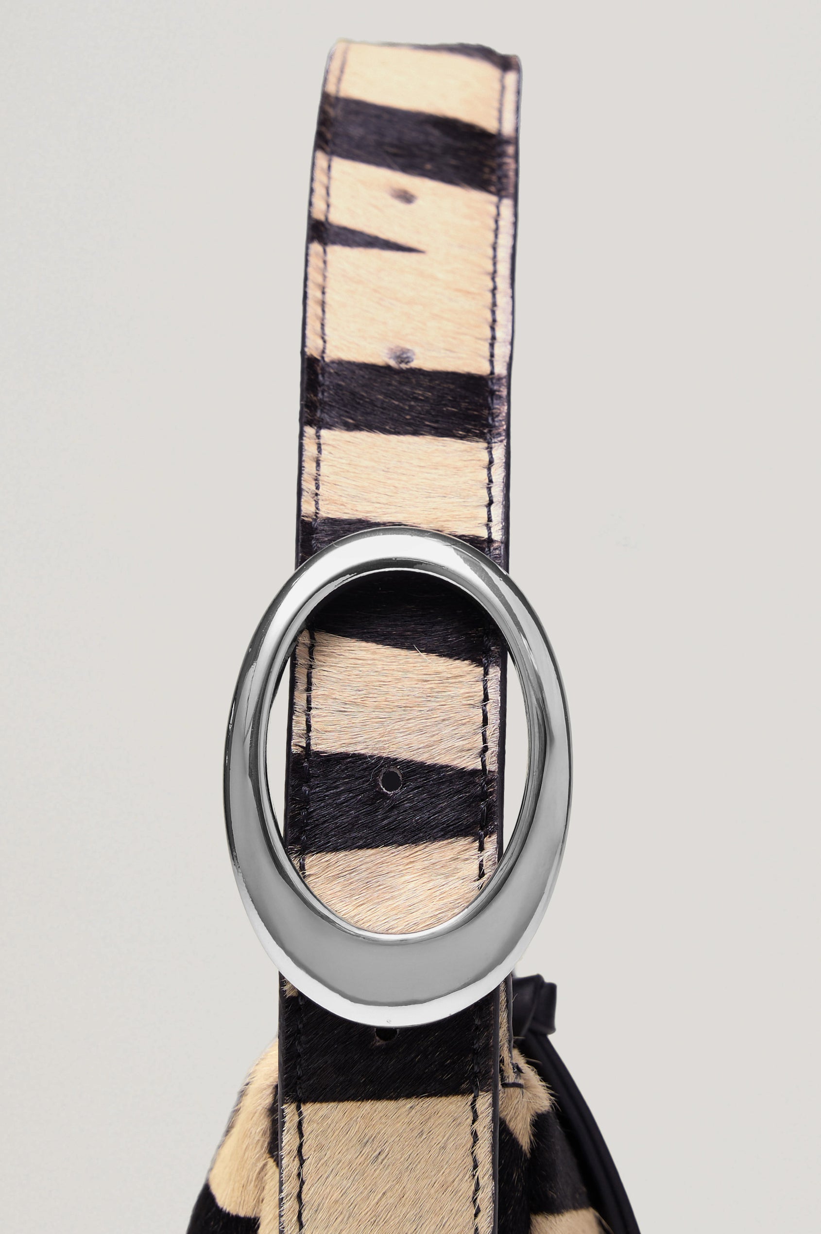 The Lucca is a long-hair cowhide shoulder bag with an adjustable strap and polished silver oval buckle. In Zebra Haircalf colorway. Front view featured.