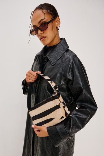The Lucca is a long-hair cowhide shoulder bag with an adjustable strap and polished silver oval buckle. In Zebra Haircalf colorway. Side view modeled on the shoulder featured.