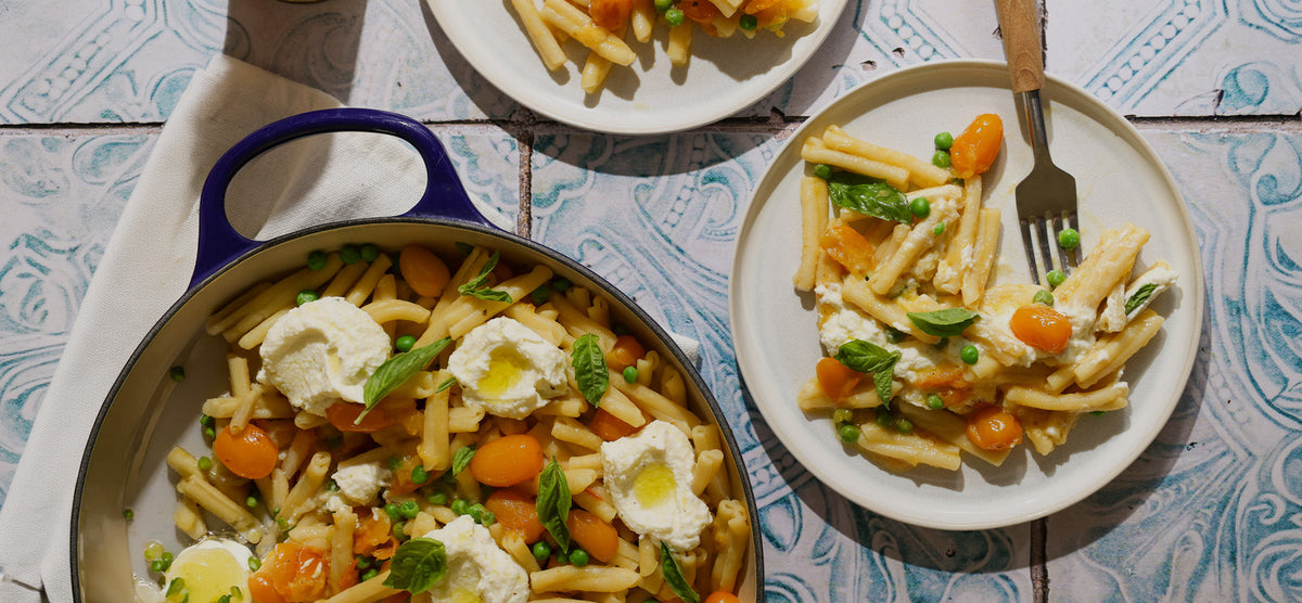 Pasta dish with cheese and vegetables on a plate and in a pan, served on a tiled table.