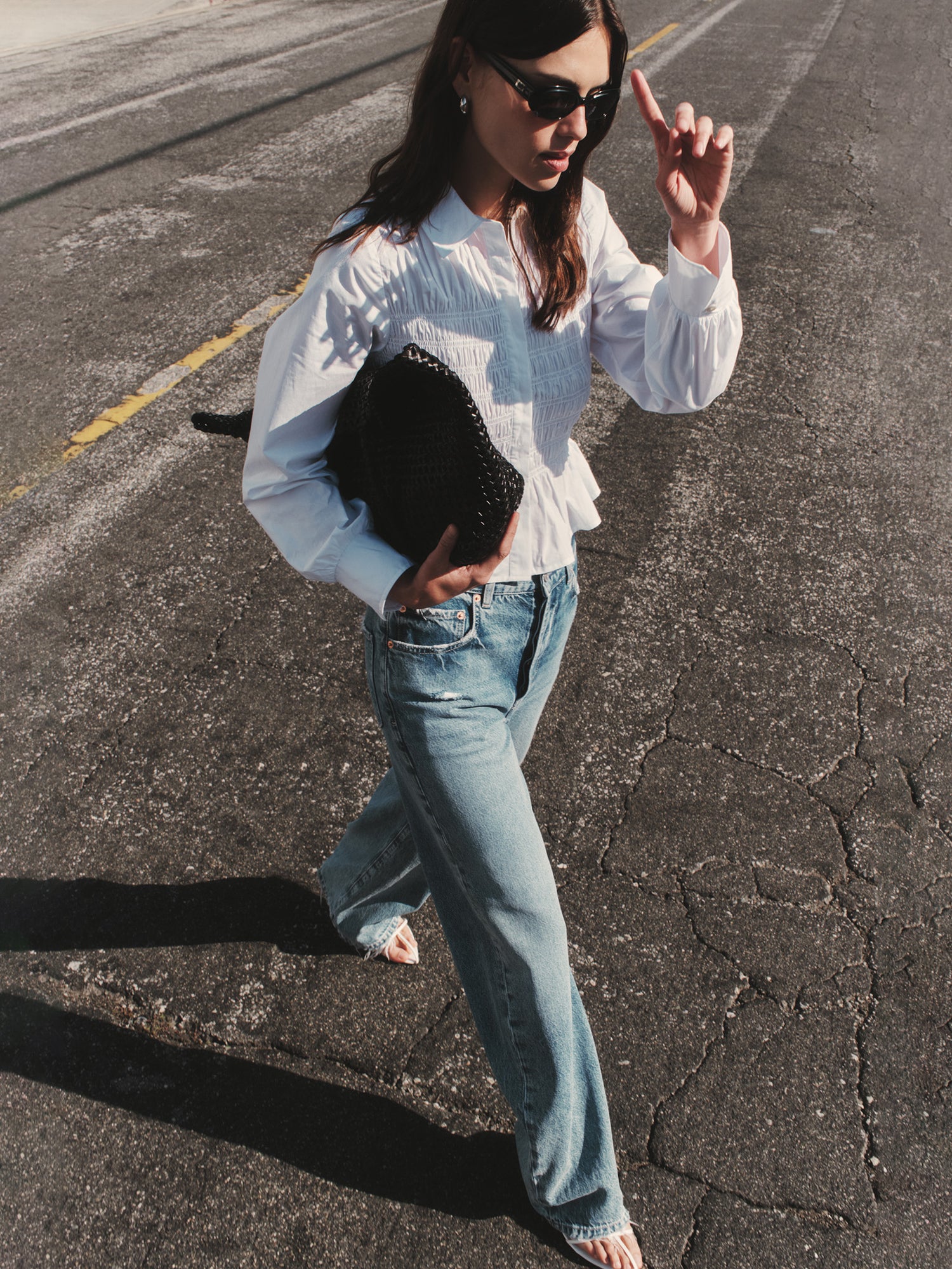 Woman in white blouse and blue jeans holding a black clutch on a road.