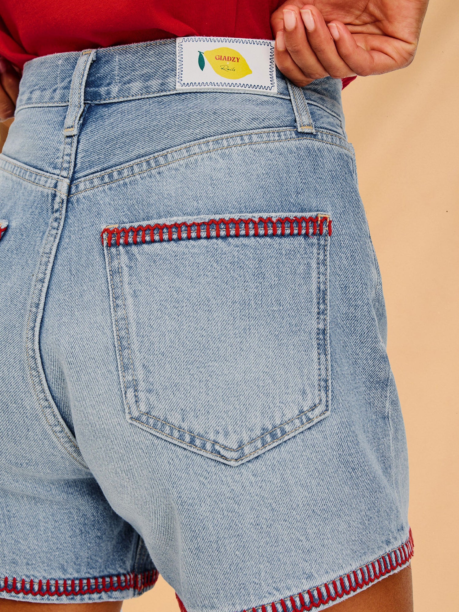 Light blue denim shorts with red stitching on a beige background