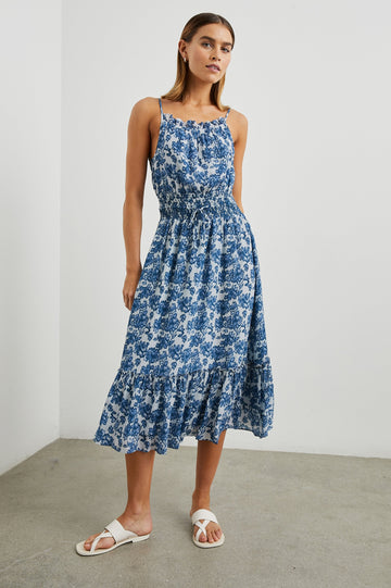 Magdalene Sleeveless Midi Dress with Spaghetti Straps, a Button Keyhole at the Back, a Shirred Waist with a Drawstring, a Scoop Neckline with Ruffled Trim, and a Ruffled Hem in Chambray Floral Colorway, Blue Flowers on White - Front Full Body View Featured on Model  