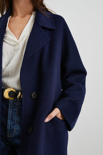 Marta Knee-Length Coat with Two Button Closure, Notched Lapels, Two Front Flap Pockets, and a Tie Belt in Navy Colorway - Front View Featured on Model 