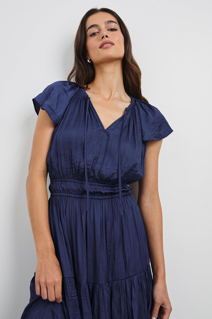 Mirielle Midi Dress with Short Flutter Sleeves, Split V-Neck with Self Tie and an A-Line Tiered Skirt in Admiral Blue Colorway. Front View Shown on Model.