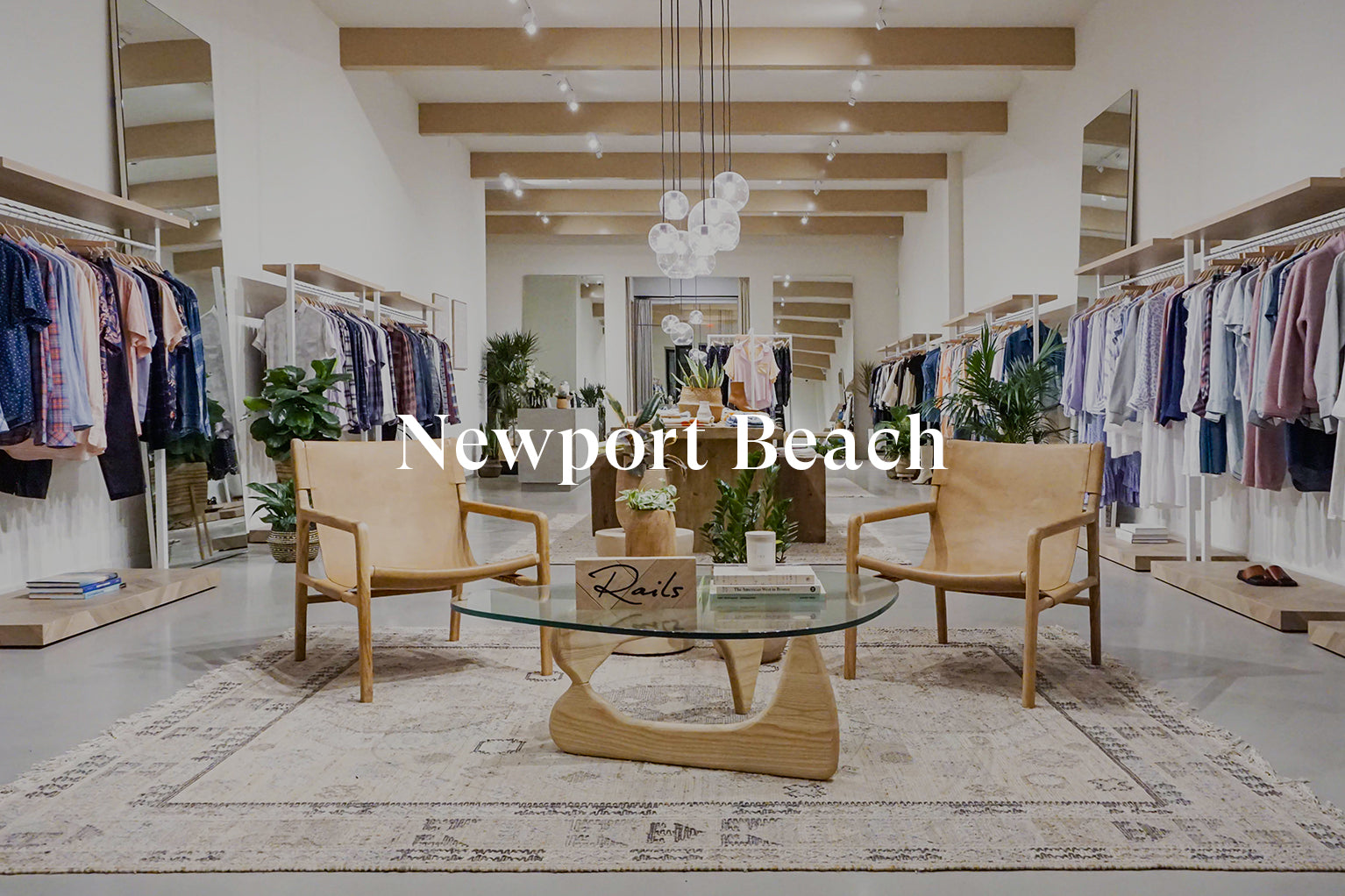 INSIDE OF NEWPORT BEACH STORE SHOWING MULTIPLE CLOTHING RACKS FULL OF CLOTHES AGAINST EACH WALL AND TWO CHAIRS IN THE MIDDLE OF THE ROOM