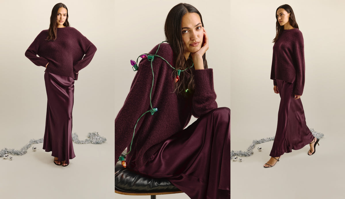 A wide triptych in a warm cream studio setting. A model wears an oversized plum knit sweater over a satin plum bias-cut maxi skirt with black strappy heeled sandals. The holiday styling includes silver tinsel, silver ornaments, and a string of vintage multicolored C9 lights draped over her shoulder in the center frame.