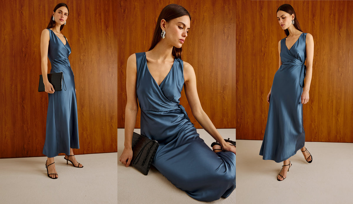 A three-panel fashion collage showing a woman modeling a satin-like sleeveless maxi dress in a dusty blue tone against a wood-paneled interior. The center panel is the main view, with the model seated slightly bent forward; side panels show full-length poses standing, one holding a black clutch.