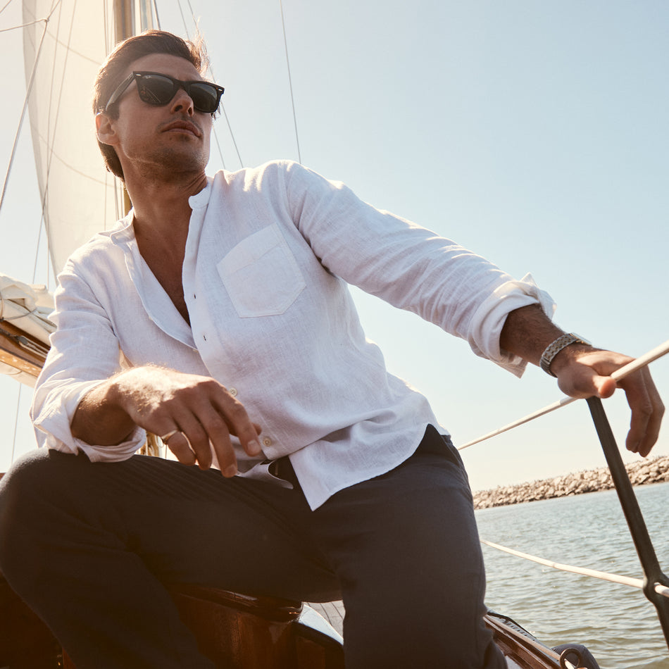 EDITORIAL IMAGE OF MODEL ON A SAIL BOAT WEARING ANTOINE SHIRT IN ANTIQUE WHITE AND CALLUM PANT IN DEEP MERIDIAN