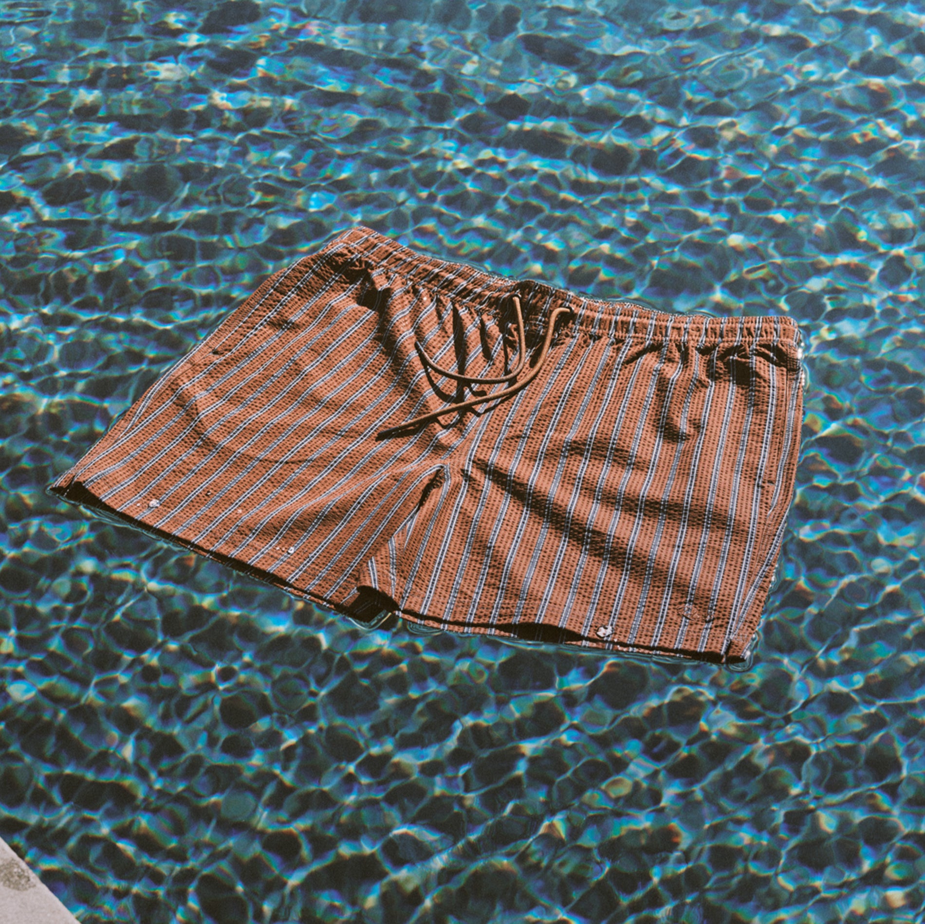 Brown striped men's swim shorts floating in a pool