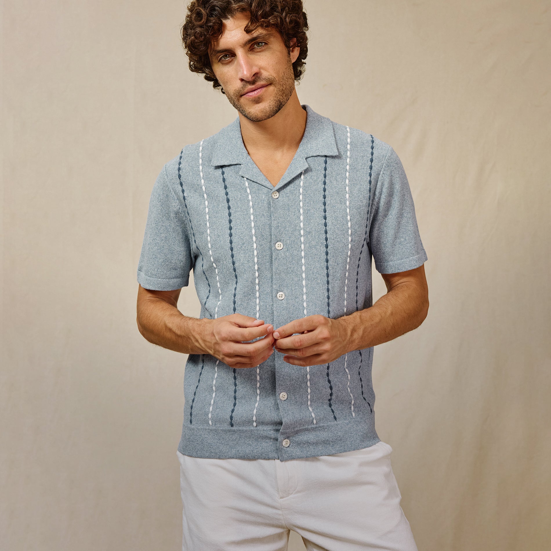 Man wearing a light blue short-sleeve shirt with white patterns on a beige background