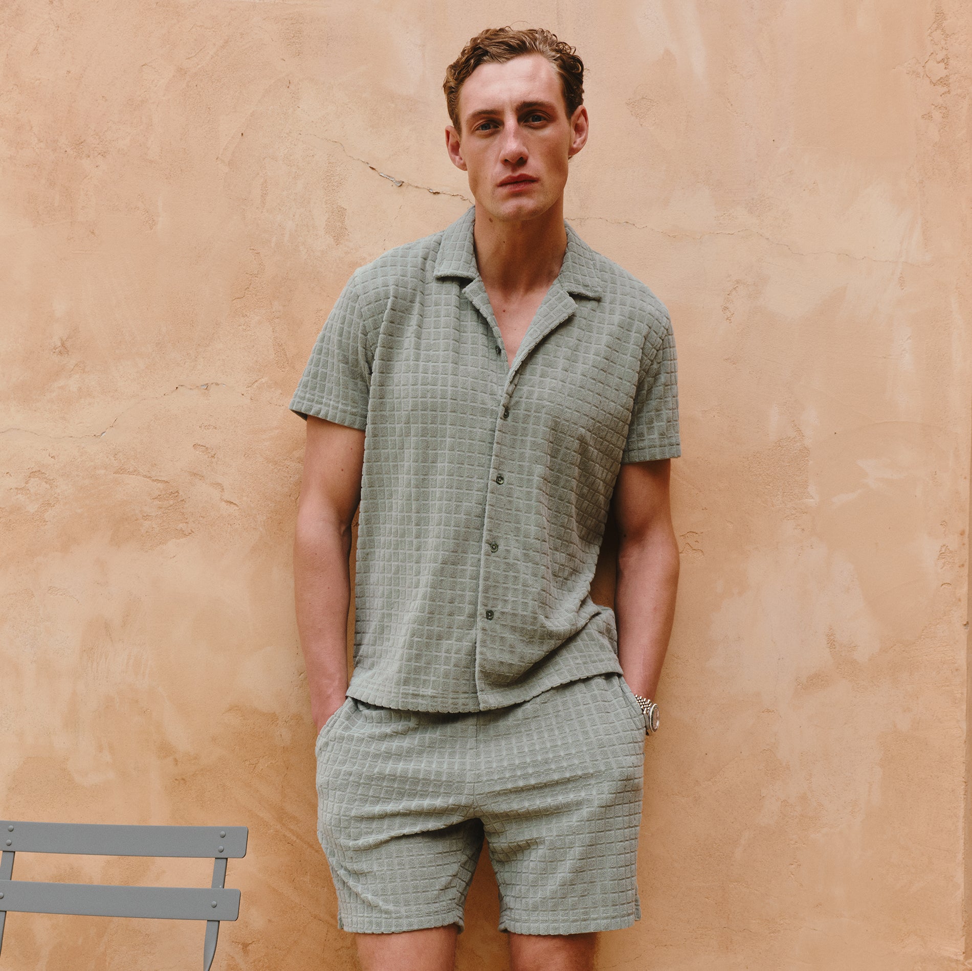 Man wearing a green checkered outfit standing against a beige wall.