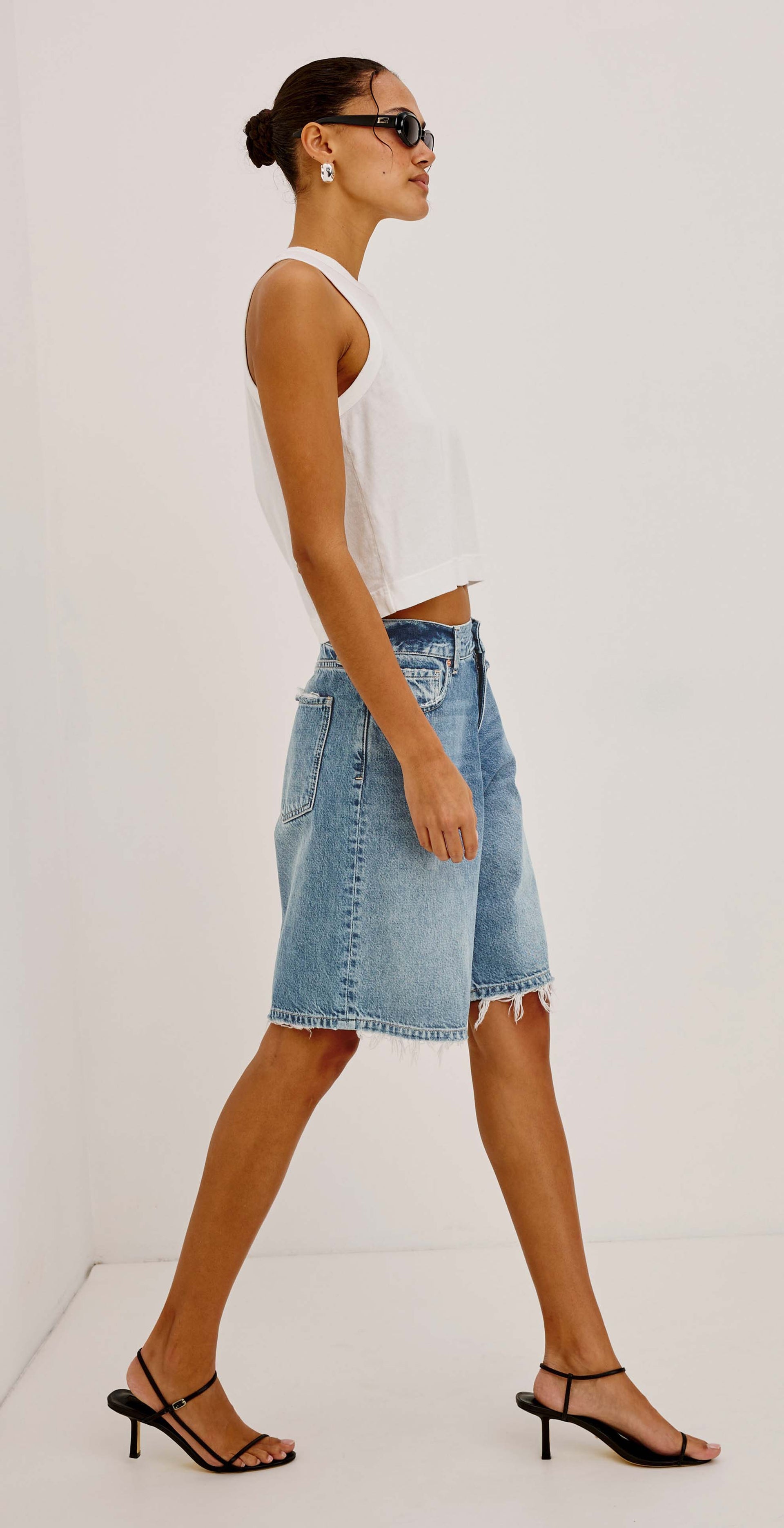 A split-view model photo showing a person wearing light-wash denim shorts with a frayed hem and a white cropped tank top against a plain light background.