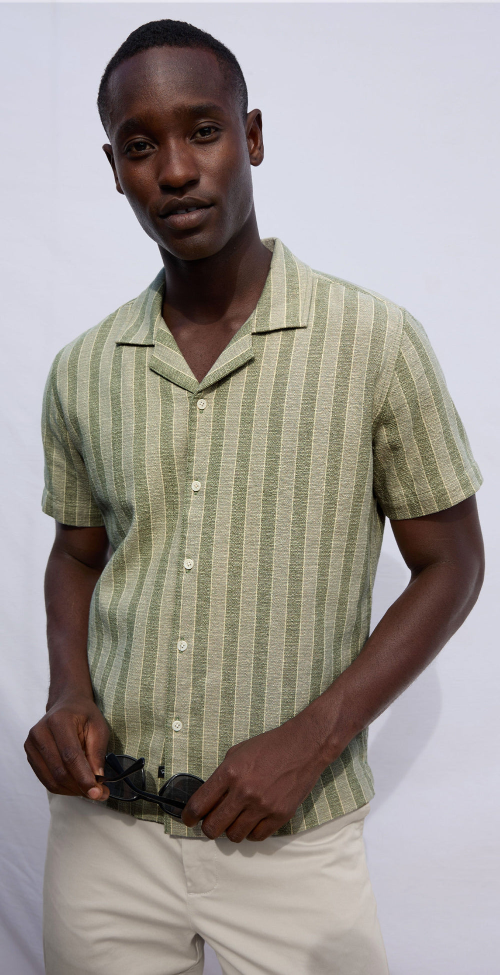 Man wearing a green striped shirt and beige pants against a white background