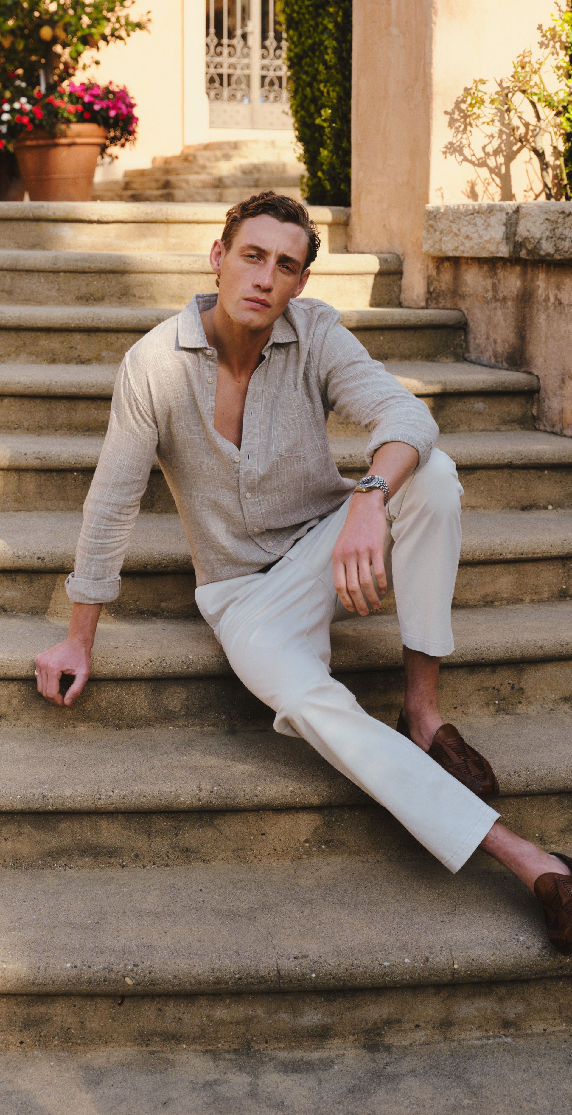 Man in beige shirt and white pants posing outdoors on stone steps.