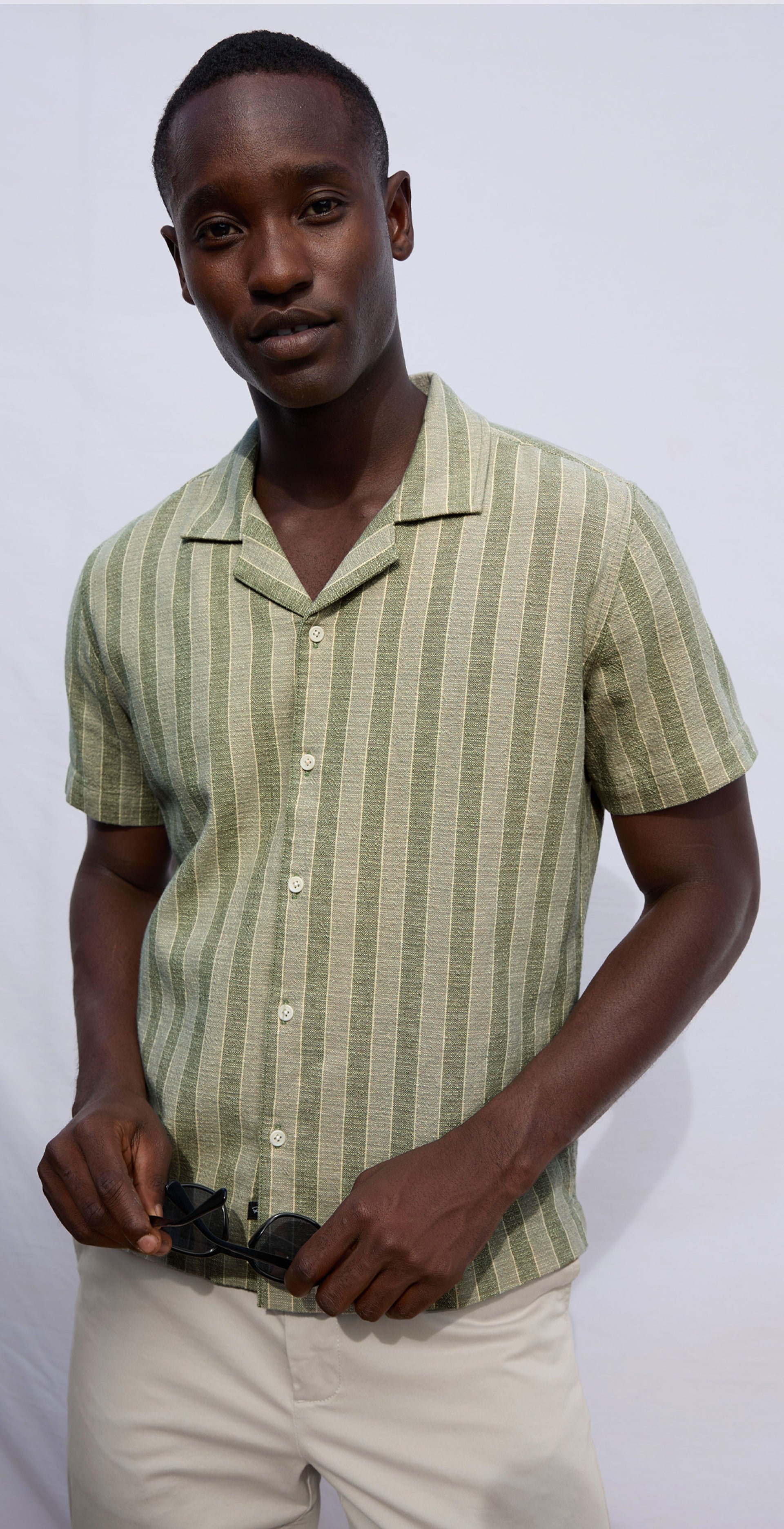 Man wearing a green striped shirt and beige pants against a white background