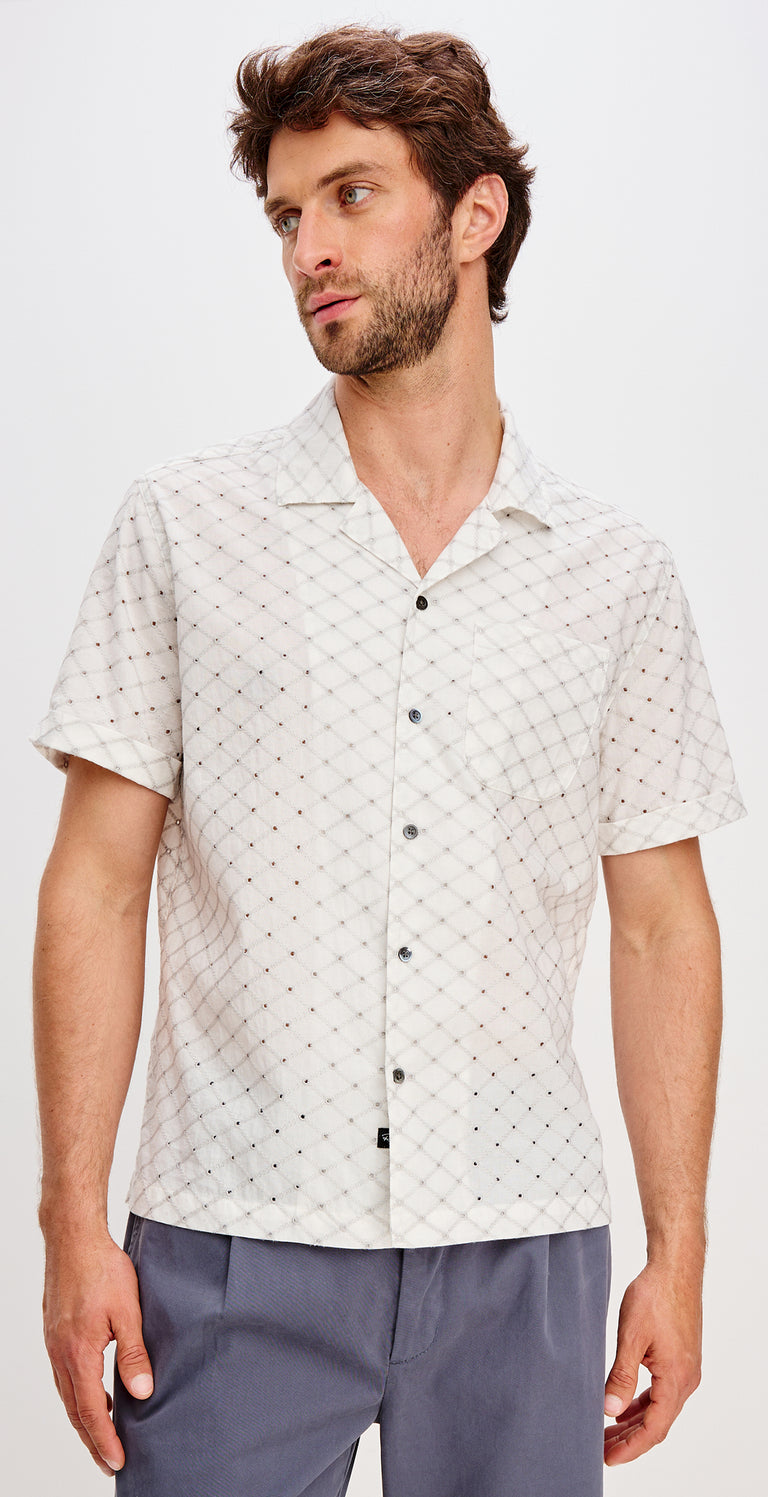 Man wearing a patterned white shirt with a plain background.