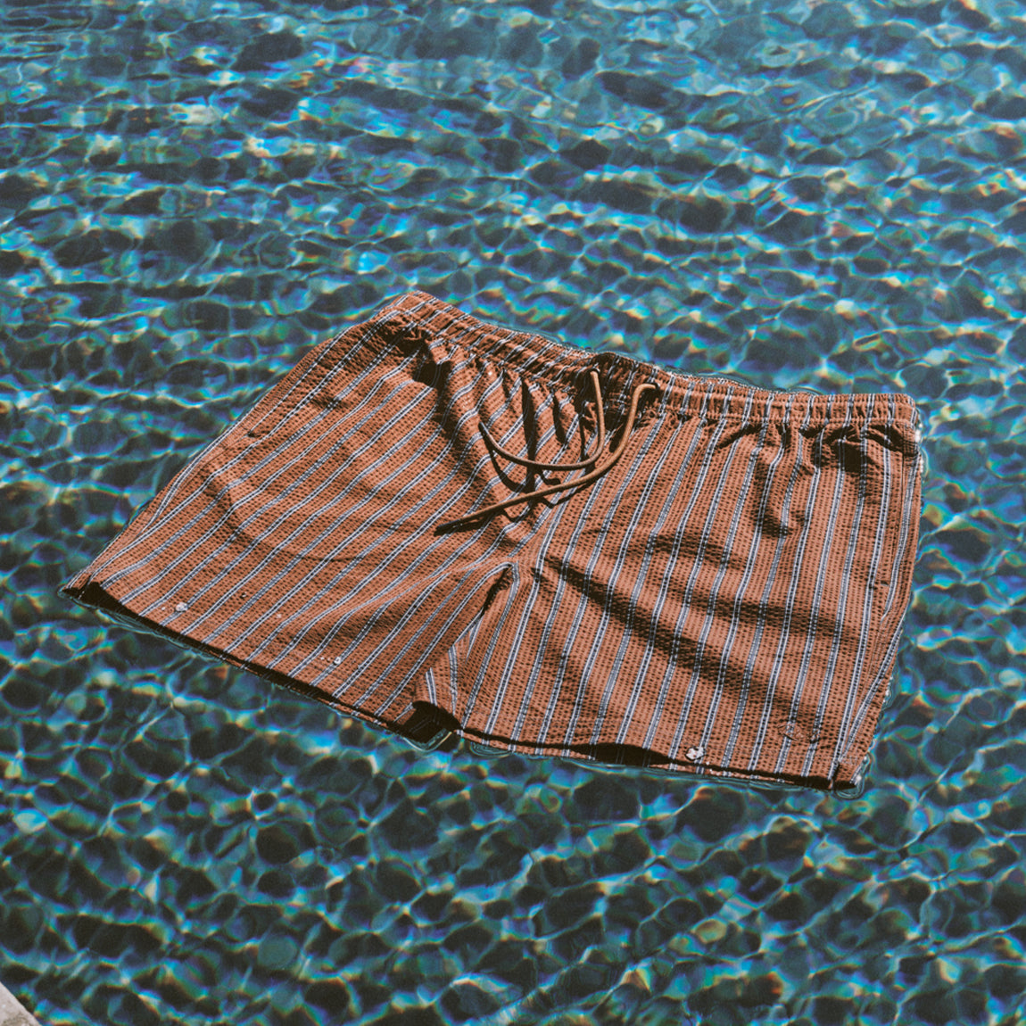 Brown striped men's swim shorts floating in a pool