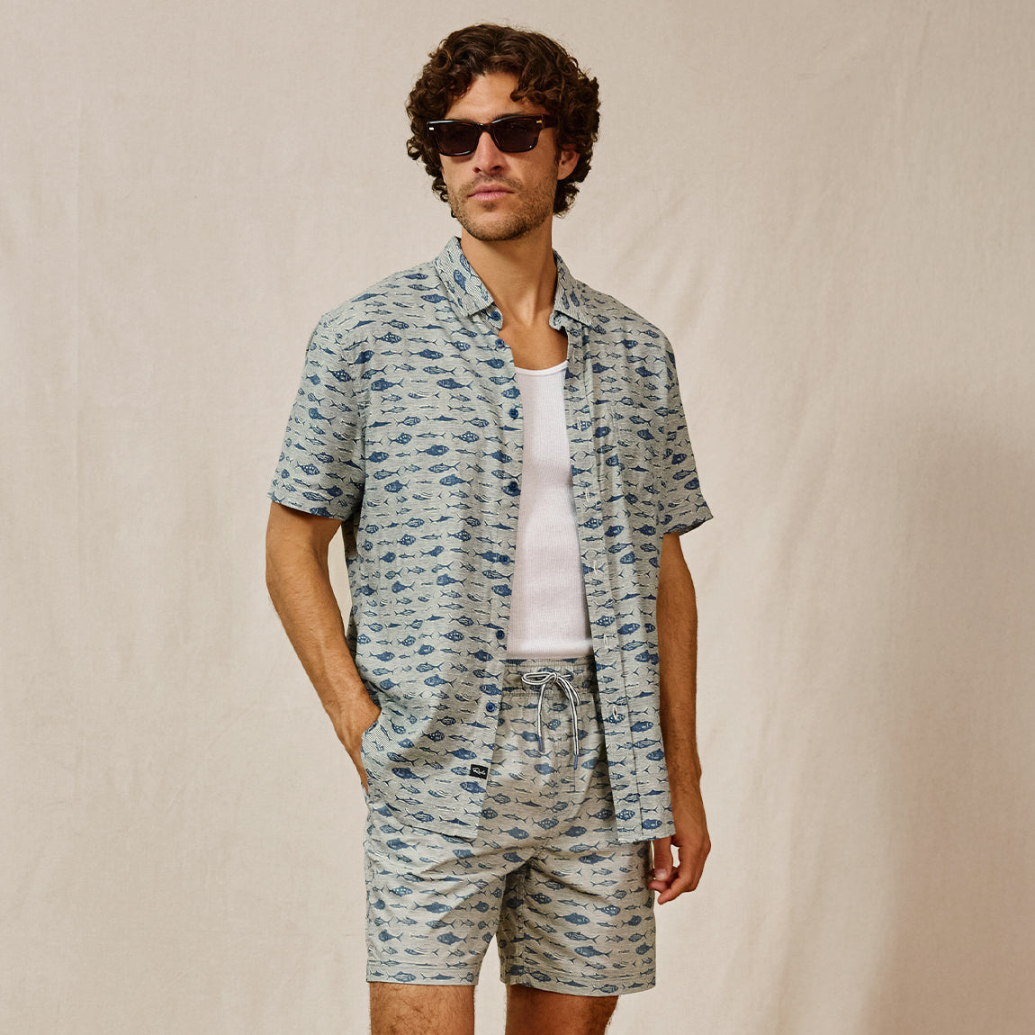 Man wearing a patterned shirt and shorts set with sunglasses on a beige background