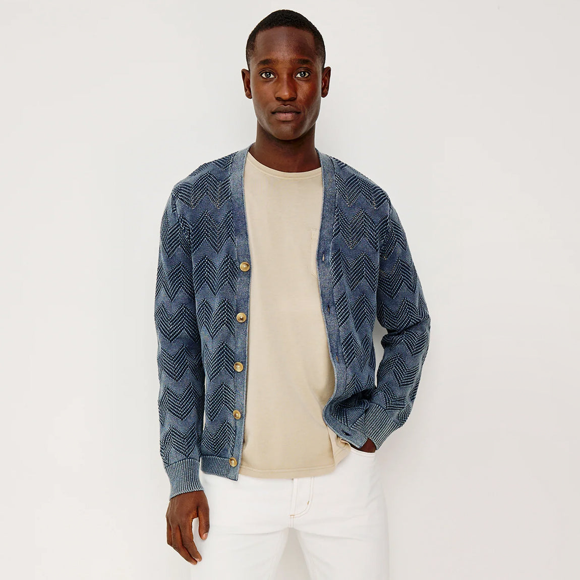 Man wearing a blue patterned cardigan over a beige shirt on a white background