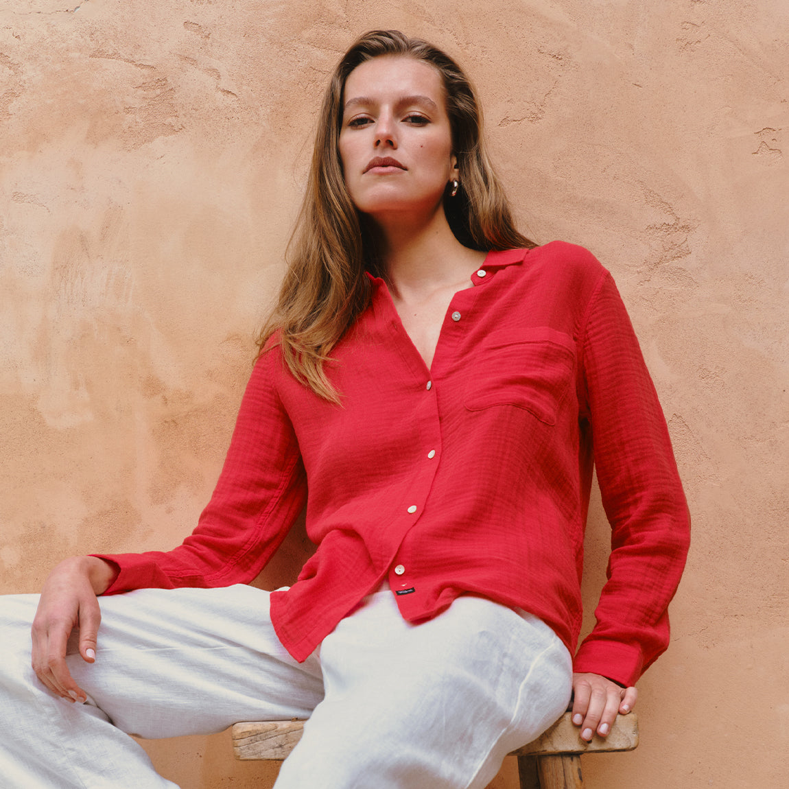 Woman wearing a red shirt sitting against a beige wall
