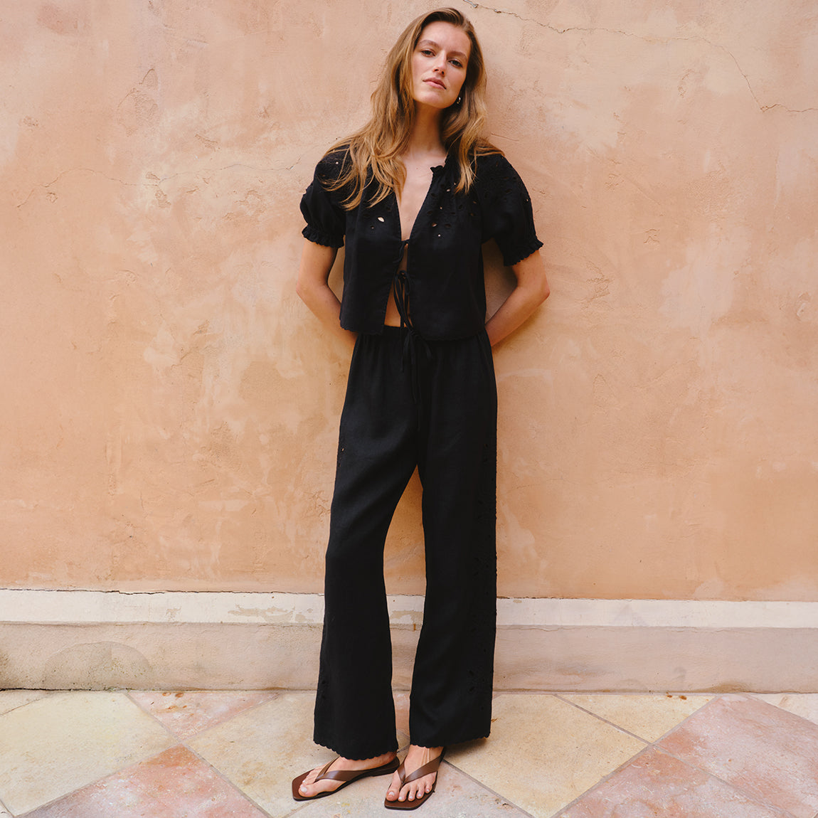 Woman wearing a black outfit against a peach-colored wall.
