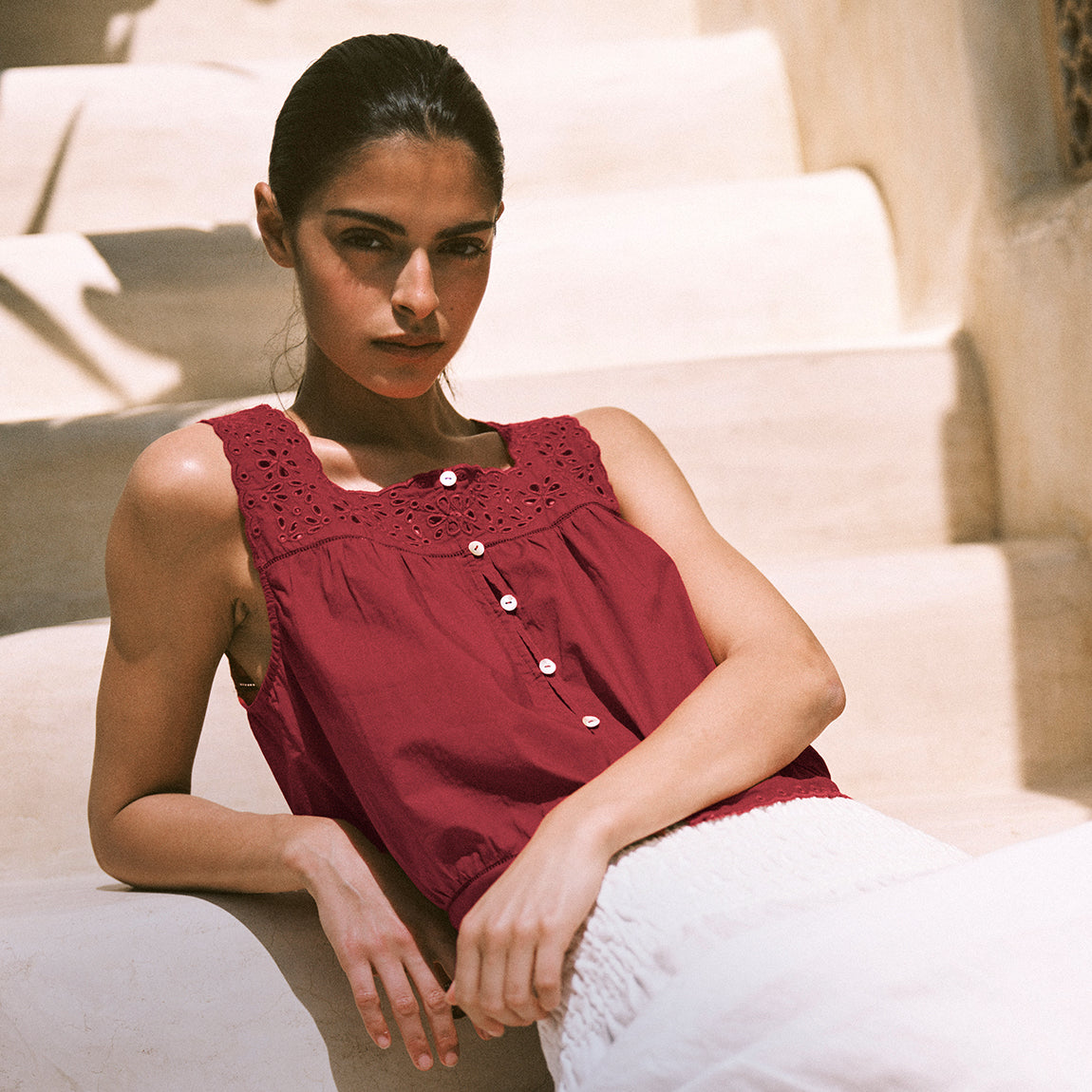 Woman wearing a red sleeveless top sitting on a staircase.