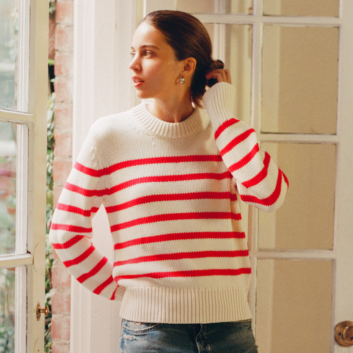Woman wearing a white sweater with red stripes indoors.