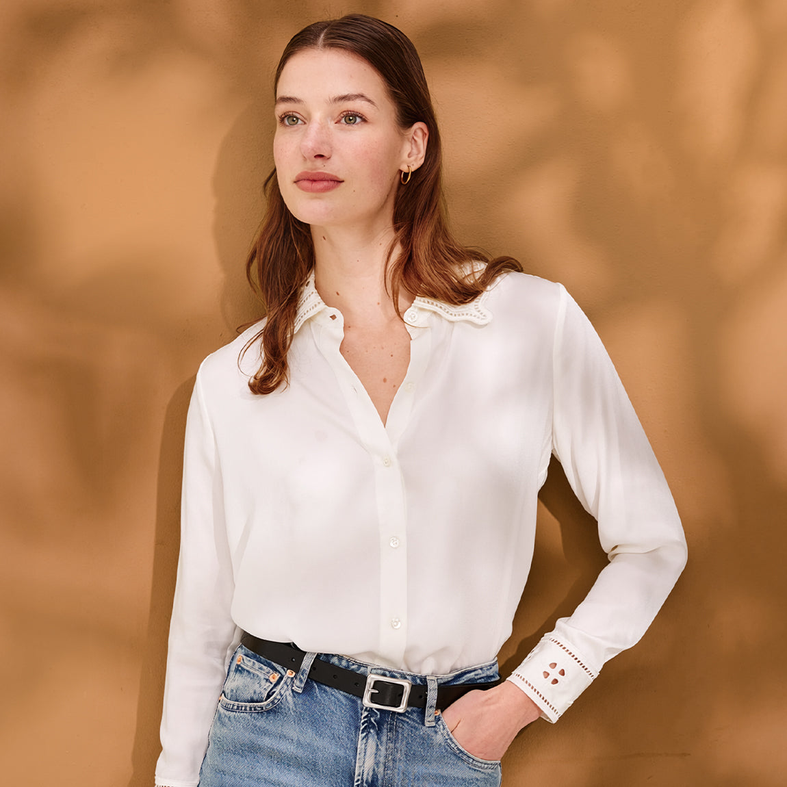 Woman wearing a white blouse and blue jeans against a warm brown background