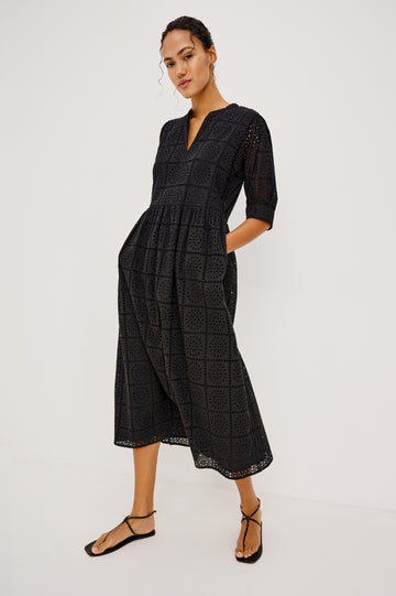 Nella Smock Maxi Dress in Cotton With Grid Eyelet Embroidery Lined Body Split Band V-Neckline Drop Waist Gathered Skirt and Short Puff Sleeves With Fitted Cuffs in Black Colorway - Full Body Front View Featured on Model