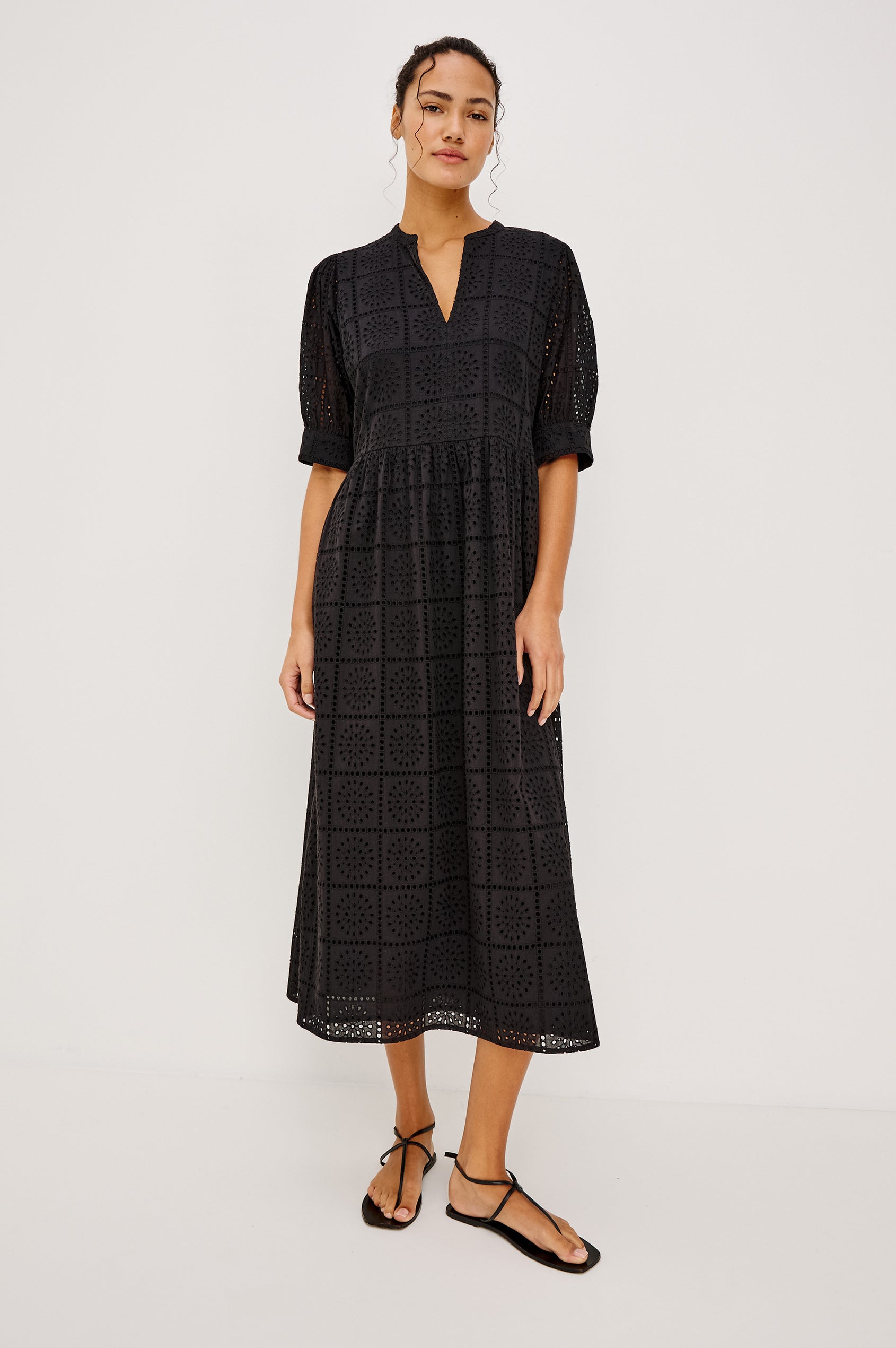 Nella Smock Maxi Dress in Cotton With Grid Eyelet Embroidery Lined Body Split Band V-Neckline Drop Waist Gathered Skirt and Short Puff Sleeves With Fitted Cuffs in Black Colorway - Full Body Front View Featured on Model