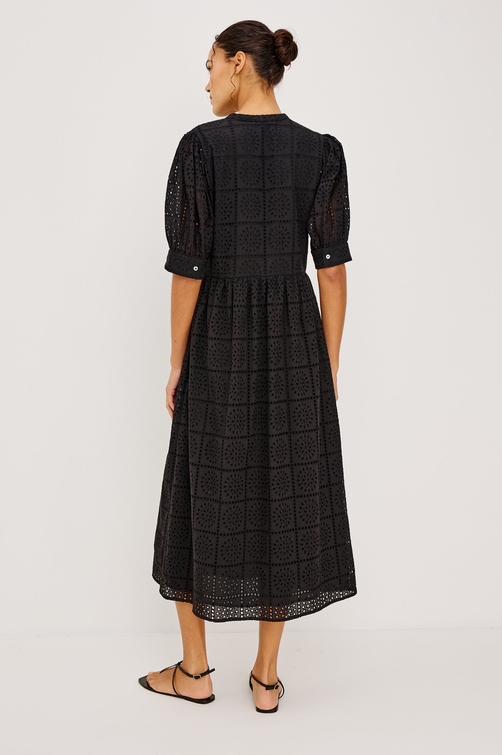 Nella Smock Maxi Dress in Cotton With Grid Eyelet Embroidery Lined Body Split Band V-Neckline Drop Waist Gathered Skirt and Short Puff Sleeves With Fitted Cuffs in Black Colorway - Full Body Back View Featured on Model