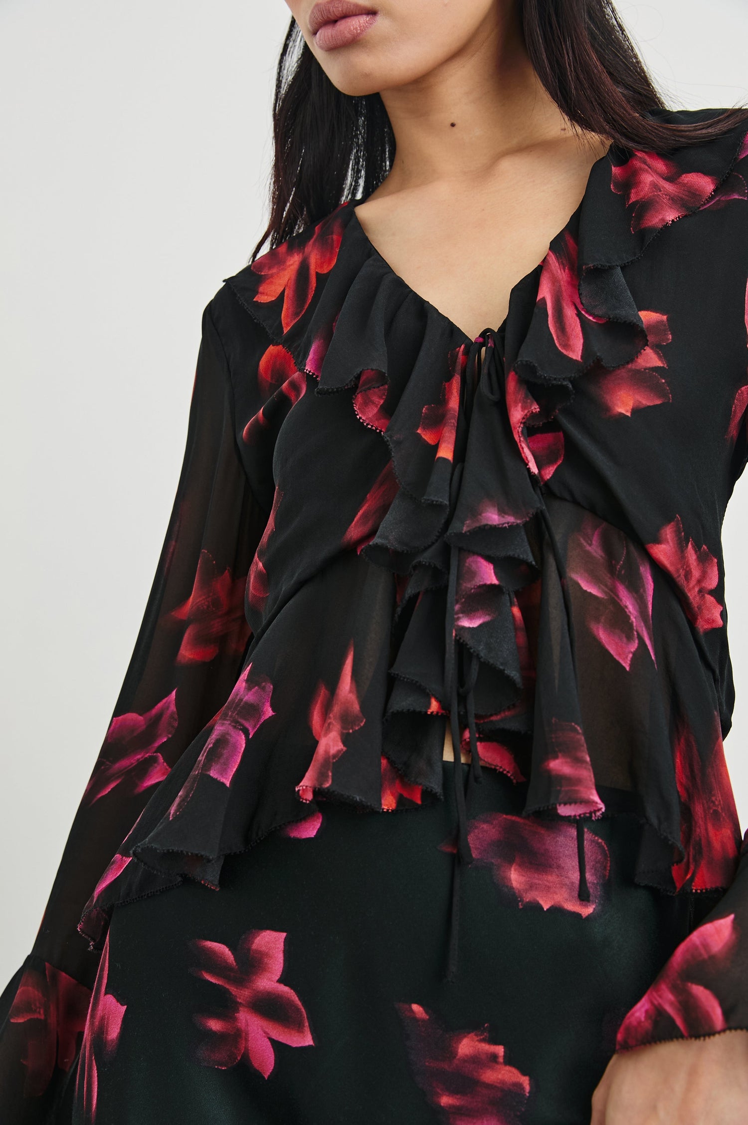 Nicoletta Long-Sleeve Semi-Sheer Top with Deep V Neck, Front Tie Closure, and Ruffled Trim in Dark Azalea Colorway, Flowers in pinks and purple on Black - Front View Featured on Model