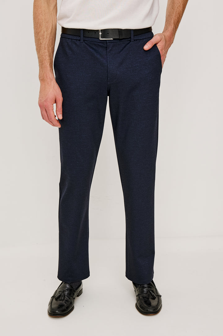 The Olivier is a trouser with a front zip fly, belt loops, side pockets, and pintuck detailing in Navy colorway. Front view featured on model.