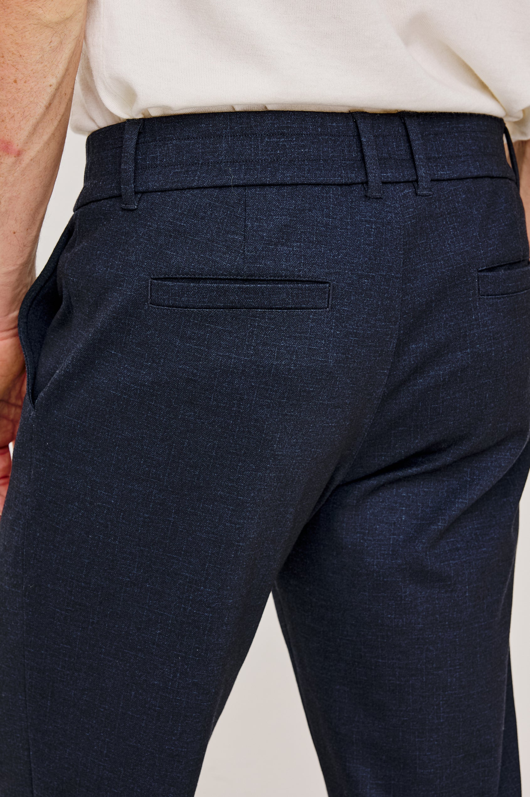 The Olivier is a trouser with a front zip fly, belt loops, side pockets, and pintuck detailing in Navy colorway. Back detail view featured on model.