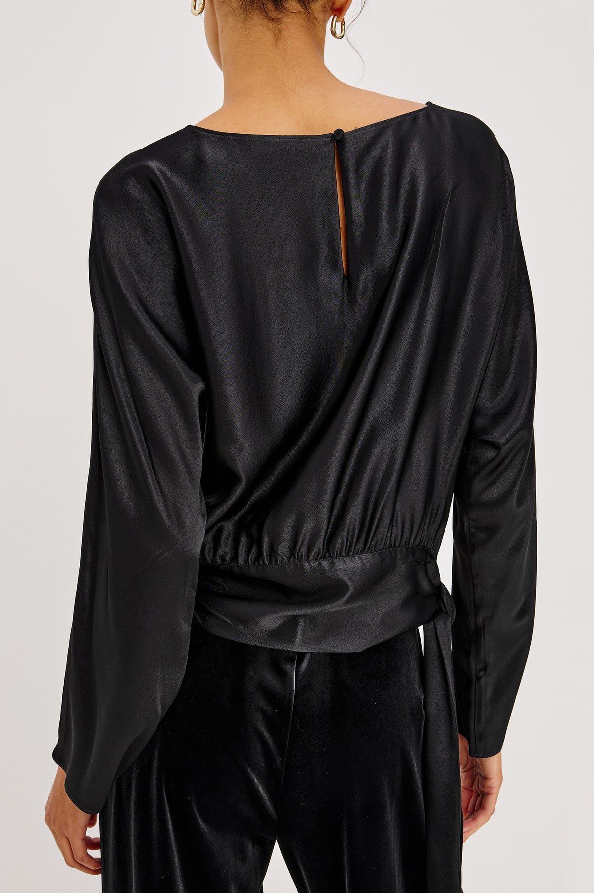 Opal Long-Sleeve Top in Luxe Satin With a Self Tie Hem in Black Colorway - Back Crop View Featured on Model.