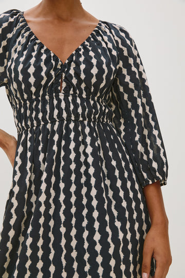 Paio midi dress with a fitted bodice, three quarter sleeves with a slight puff effect, flowing skirt, and eyelet closures at the chest in Painted Noir colorway - close up of details on model