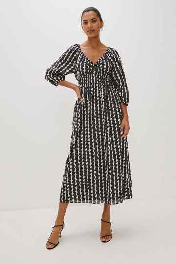 Paio midi dress with a fitted bodice, three quarter sleeves with a slight puff effect, flowing skirt, and eyelet closures at the chest in Painted Noir colorway - full body front view on model